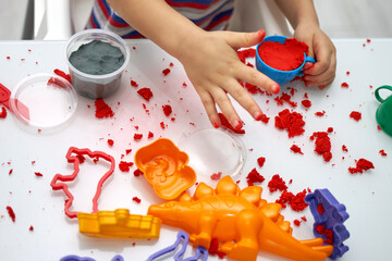A child's hands play with bright kinetic sand on a white table. An educational game of kinetic sand...