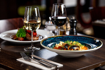 A close up of a plate of food and two glasses of wine on a table in a restaurant