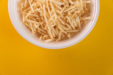 White bowl with potato straw on yellow background