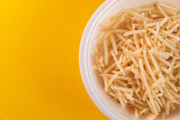 White bowl with potato straw on yellow background
