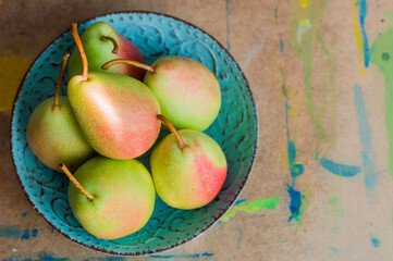 Green pears with red sides lying on a turquoise plate in the sunlight. 