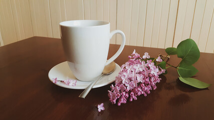 White porcelain cup of coffee  or tea with lilacs on the wooden table. Home decor and comfort concept.