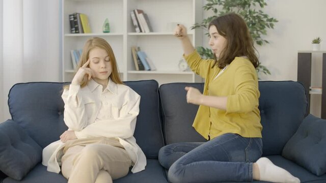 Tired teenage girl listening to emotional talkative friend, sitting on sofa