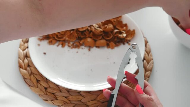 Crushing a walnut with a steel nutcracker. Walnuts in a white bowl.