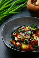 baked eel with rice and green onion on dark background closeup