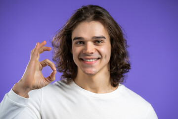 Fototapeta premium Handsome man shows okay, ok gesture. Happy guy on violet background. Winner. Success. Positive male model smiles to camera. Body language. 