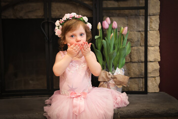 Close Up Portrait, 2 Years Old Toddler Girl with Big Blue Eyes, in light Pink Dress with Pink Flowers on her head, Sitting by the fireplace, Birthday Girl, Ukrainian Head bend, Little Princess 