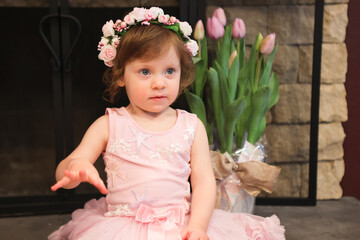 Close Up Portrait, 2 Years Old Toddler Girl with Big Blue Eyes, in light Pink Dress with Pink Flowers on her head, Sitting by the fireplace, Birthday Girl, Ukrainian Head bend, Little Princess 