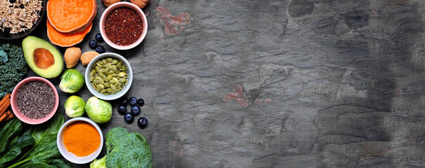 Group of healthy food ingredients. Top view side border on a slate banner background. Copy space. Super food concept with green vegetables, berries, whole grains, seeds, spices and nutritious items.