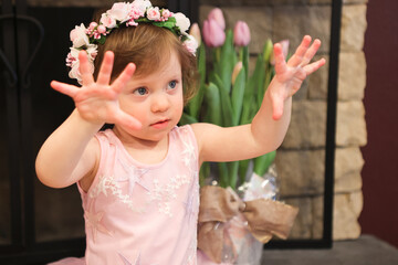 Close Up Portrait, 2 Years Old Toddler Girl with Big Blue Eyes, in light Pink Dress with Pink Flowers on her head, Sitting by the fireplace, Birthday Girl, Ukrainian Head bend, Little Princess 