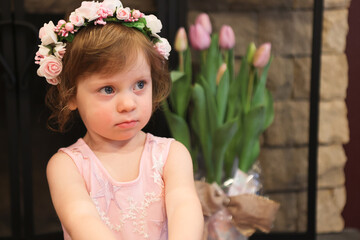 Close Up Portrait, 2 Years Old Toddler Girl with Big Blue Eyes, in light Pink Dress with Pink Flowers on her head, Sitting by the fireplace, Birthday Girl, Ukrainian Head bend, Little Princess 