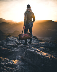 man with travel bag on mountain top enjoying sunset