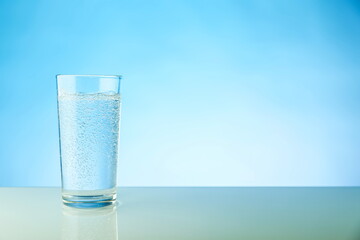 glass of sparkling water on blue background with copy space. mineral water with gas bubbles in a glass on a light blue background 