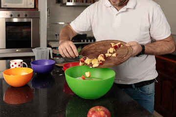 Caucasian man, between 30-39 years old, adding apple inside a bowl with a preparation .