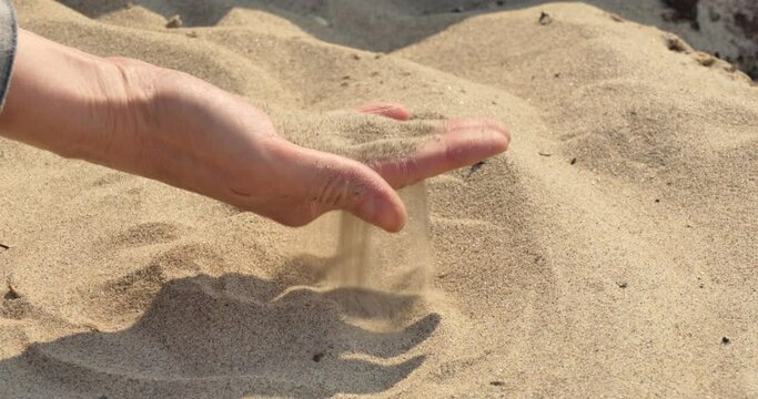 Hand in the sand. A woman strokes the sand on the beach and pours it through her fingers. Closeup. 