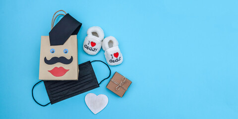 Shopping bag, mask and baby shoes on blue.