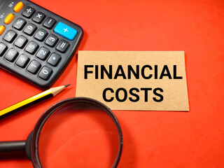 Selective focus of calculator,pencil and magnifying glass with text FINANCIAL COST on red background.Business concept.