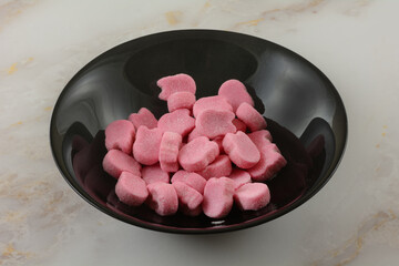 Pink raspberry gummy candy pieces in black bowl on table