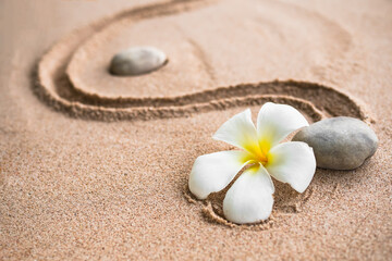 Fototapeta na wymiar Japanese zen garden stone on sand beach. rock or pebbles with plumeria flowers with copy space. for aroma therapy spa on summer holidays. meditation wellness and tranquility Japanese concept.