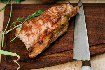 Grilled pork breast on a wooden board with a knife.