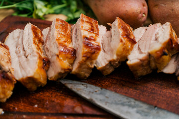 Grilled pork breast cut into strips on a wooden board with a knife.