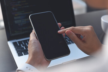 Mockup image of woman hand using blank screen mobile phone during working on laptop computer on office table