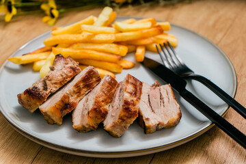 Grilled pork breast cut into strips on a plate with french fries.