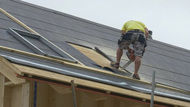 COPY SPACE Builder stands atop an unfinished roof and saws an opening in the wood before contractors mount a skylight. Worker uses a chainsaw to cut out a piece of the timber roofing for a roof window