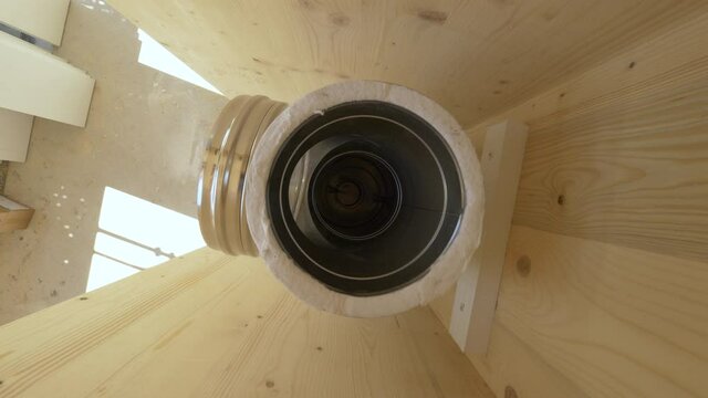 TOP DOWN, CLOSE UP: Unassembled metal chimney tubing runs along a cross-laminated timber wall panel of a contemporary housing project under construction. Detailed view down the unfinished chimney pipe