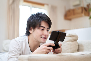 部屋でスマホゲームをプレイするアジア人男性