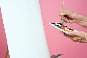 Artist's hand paints palette easel for drawing training pink background