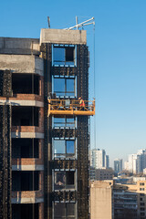 High rise construction work. Construction site workers in cradles working with facade. Suspended...