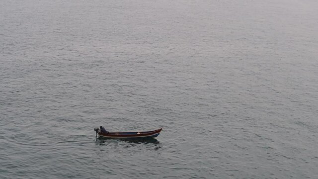A single man on a small engine boat heading out to the ocean for fishing