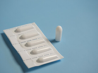 Suppository for anal or vaginal use on a blue background. Candles for the treatment of hemorrhoids,...