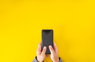 Top view of male hand holding smartphone with yellow color background with copy space.