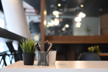 White office desk with pencil holder, plant and coffee cup at office interior