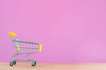 Shopping cart toy from the supermarket on table with pink background, Sale buy mall market shop consumer concept. Copy space