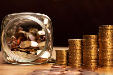 A half empty jar of coins with coin piles and more coins on a table. Save money concept banner