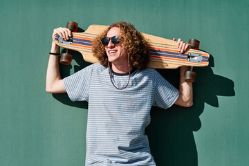 a young hipster man looking to the sun with sunglasses and a longboard or skate in his shoulders