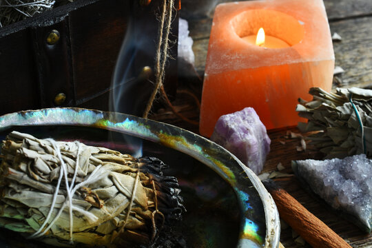 A close up image of a burning white sage bundle in an abalone shell. 