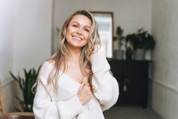 Blonde smiling woman 35 year clean fresh face and hands with long hair in cozy knitted cardigan at...