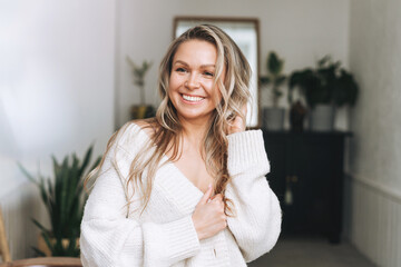 Blonde smiling woman 35 year clean fresh face and hands with long hair in cozy knitted cardigan at...