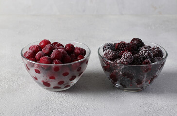 Frozen cherries and blackberries in glass transparent bowls on gray concrete background