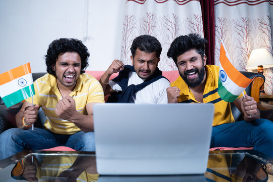 Three Young People Supporting Indian Team By Holding Indian Flags While Watching Live Streaming Cricket Match On Laptop