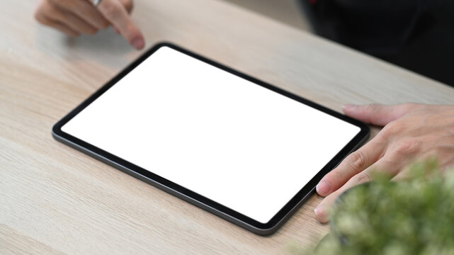 Close up view of man usig digital tablet on wooden table.