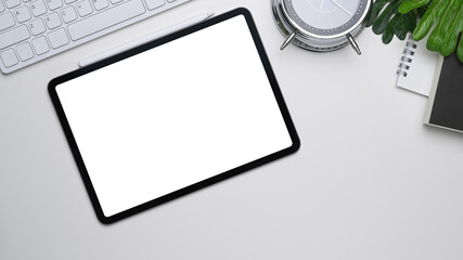 Above view of digital tablet with empty screen, notebook and key board on white office desk.