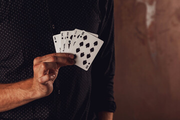 Close-up portrait of young man with gambling cards. Handsome guy throws up  with card. Clever hands of magician on brown texture background. Concept of entertainment and Hobbies. Copy space for site
