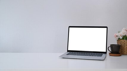 Fototapeta premium Mock up computer laptop with blank screen, coffee cup and flowers pot on white table. Copy space for products display montage.