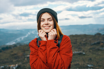 happy woman in a red jacket with a backpack and in a hat mountains in the background fresh air