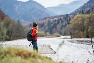 young traveler with a backpack in jeans and a sweater near the river in the mountains